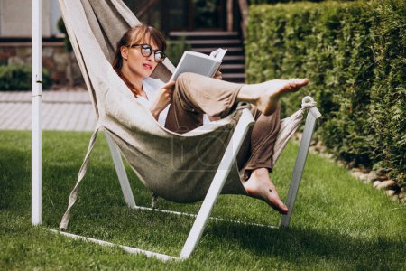 Téléchargez les photos : Femme lisant un livre dans le jardin près de la maison - en image libre de droit