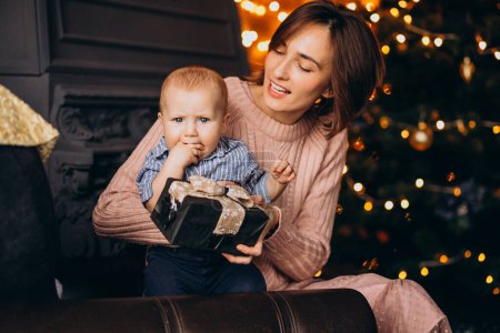 Photo for Mother with her little son unpacking gift by Christmas tree - Royalty Free Image
