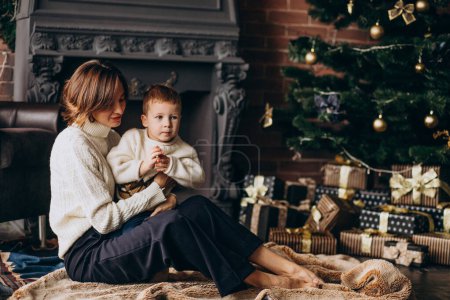 Téléchargez les photos : Mère avec son petit fils assis près du sapin de Noël - en image libre de droit