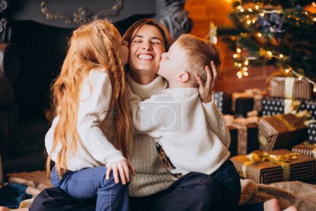 Foto de Madre con dos hijos sentados junto al árbol de Navidad - Imagen libre de derechos