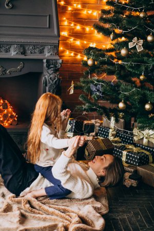 Foto de Madre con hija acostada junto al árbol de Navidad - Imagen libre de derechos