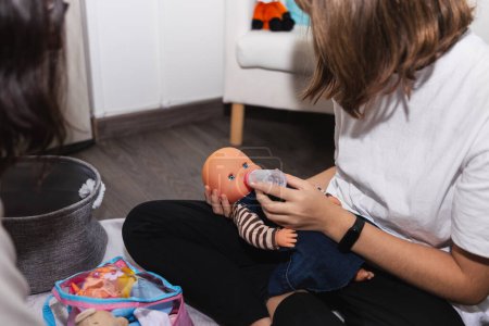 Photo for Unrecognizable preadolescent girl playing with a baby doll and bottle-feeding with her female psychotherapist. Concept of symbolic play, therapy and childhood - Royalty Free Image