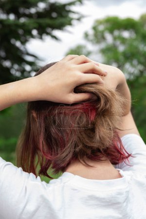 Photo for Close up portrait of a teenage girl on her back with her hands holding part of her abundant dyed hair with red locks outdoors. Concept of hair coloring, highlights and haircut. Beauty and fashion - Royalty Free Image