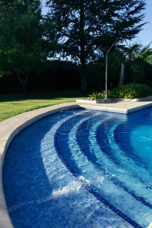 Photo for Vertical view of a swimming pool in a private garden with jets pumping water on a sunny summer day. Summer concept, heat and water - Royalty Free Image