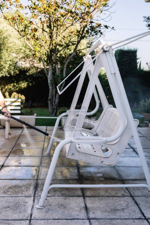 Photo for Young girl hand cleaning garden rocking chair with pressurized water machine in summer. Summer concept and housework - Royalty Free Image