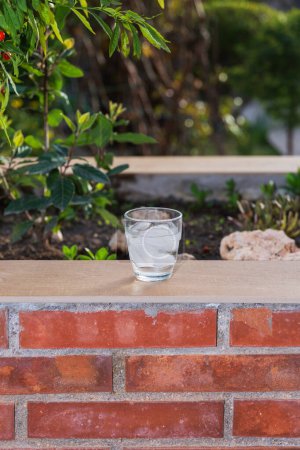 Vista frontal de un vaso lleno de hielo y agua en una pared de ladrillo en una terraza. Afuera, noche de verano. Concepto de verano, calor y bebida refrescante