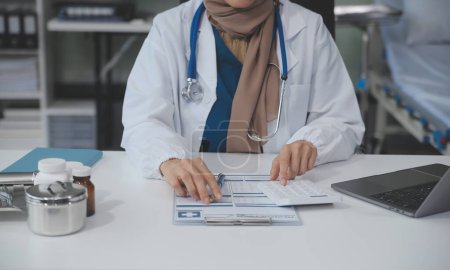 Téléchargez les photos : Médecin femme assise au bureau et rédigeant une ordonnance pour sa patiente - en image libre de droit