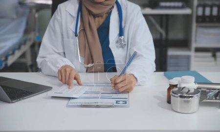 Female doctor sitting at desk and writing a prescription for her patient