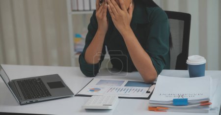 Asian women sitting in a home office With stress and eye strain.Tired businesswoman holding eyeglasses and massaging nose bridge. There are tablets, laptops, and coffee.