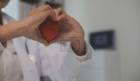 Hands of doctor woman holding red heart, showing symbol of love, human support to patient, promoting medical insurance, early checkup for healthcare, cardiologist help. Close up of object