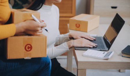 Asiatische KMU-Geschäftsfrauen nutzen Laptop-Computer, um die Online-Versandboxen ihrer Kunden zu Hause zu überprüfen. Starting Small Business Entrepreneur KMU freiberuflich. Online-Geschäft, Work at Home Konzept.