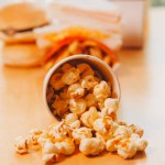 A bucket of popcorn, top-view, warm colors, light brown wooden background, flat lay, daylight macro close-up