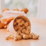 A bucket of popcorn, top-view, warm colors, light brown wooden background, flat lay, daylight macro close-up