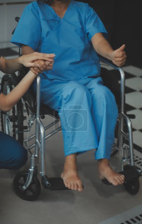 Foto de Doctor dando esperanza. Primer plano de la joven médica inclinada hacia adelante a la sonriente paciente anciana sosteniendo su mano en las palmas de las manos. Mujer cuidadora en bata blanca apoyando a anciana alentadora - Imagen libre de derechos