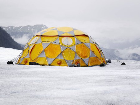 Foto de Tienda de campaña naranja-gris en el paisaje helado. Montañas rocosas crestas y nubes bajas en el fondo - Imagen libre de derechos