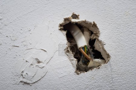 Foto de Pared dañada con cables eléctricos expuestos dentro de una casa residencial durante el día - Imagen libre de derechos