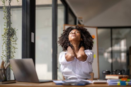 Foto de Mujer negra físicamente activa por fatiga sentada en un escritorio. cansada del trabajo, Torsión por dolor, Síndrome de oficina de los trabajadores de oficina - Imagen libre de derechos