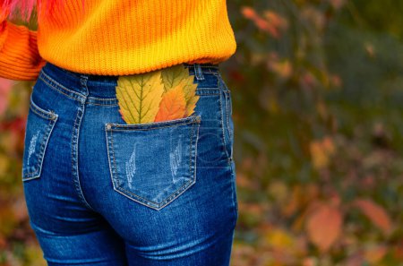 Foto de Una mujer está de pie con la espalda en un bosque otoñal, hojas rojas y amarillas sobresaliendo de su ropa. Explorando la naturaleza del otoño dorado. - Imagen libre de derechos