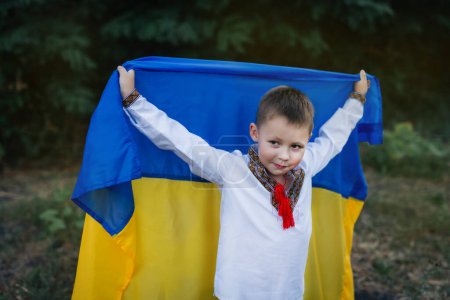 Unabhängigkeitstag der Ukraine. Ein kleiner Junge in weißem Hemd mit gelb-blauer Fahne der Ukraine auf dem Rasen. Flagge der Ukraine. Tag der Verfassung.