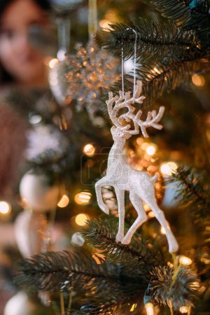 Photo for Close-up of Christmas toys on the tree. A golden deer hangs on the branch of the Christmas tree. Bokeh garlands in the background. New year concept. - Royalty Free Image