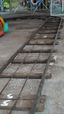 The floor train tracks in the playground are made of iron in a dirty condition mounted on several wooden sleepers