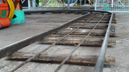 The floor train tracks in the playground are made of iron in a dirty condition mounted on several wooden sleepers