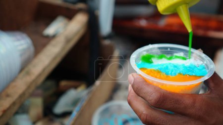 vendedores ambulantes preparan colorido hielo afeitado en vasos de plástico para los clientes