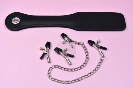 Photo for Silver nipple clips and spanking device on a pink background, slave spank paddle, accessories for adult sexual games, sex toys for BDSM, adult whip - Royalty Free Image