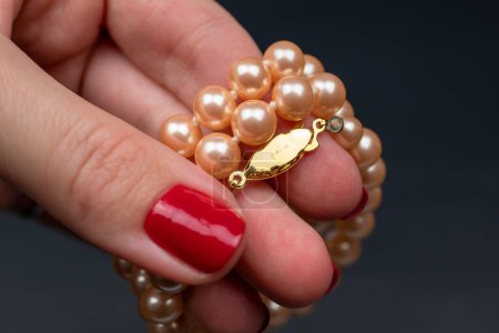 Female hand with red manicure holding a pearl necklace on dark background