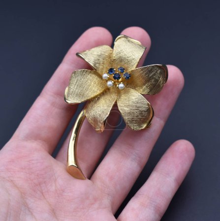 Hand holding a golden hair clip with a flower on a dark background