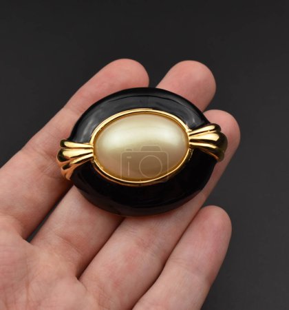 Hand holding a black and gold brooch on a dark background