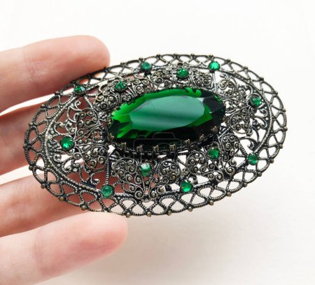 Green emerald in a silver brooch on a white background.