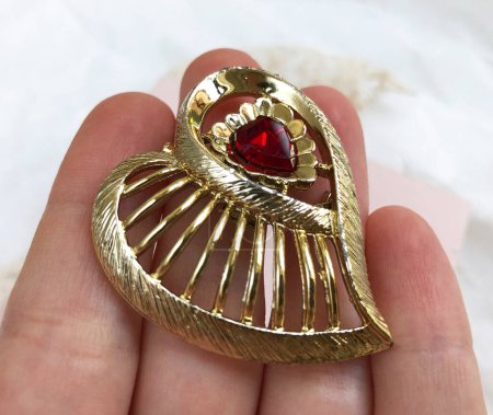 golden brooch with a red heart in the palm of your hand