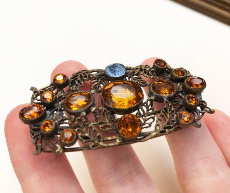 Hand holding a metal brooch with colored stones on a white background