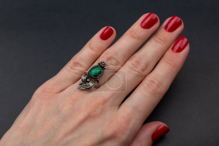 Téléchargez les photos : Main féminine avec manucure rouge tenant un anneau vert émeraude sur fond noir - en image libre de droit