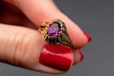 Ring with amethyst in the hand of a girl on a gray background