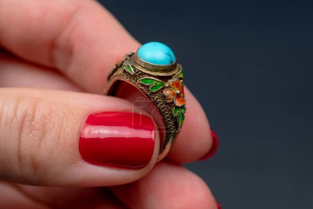 Weibliche Hand mit roter Maniküre hält einen Ring mit blauem Edelstein