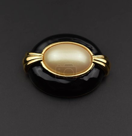 Black and gold brooch with pearls on a black background.