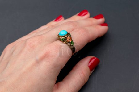 Weibliche Hand mit roter Maniküre hält einen Ring mit blauem Edelstein