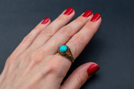 Female hand with red nail polish holding a ring with blue gemstone