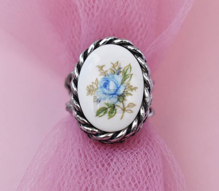 Jewelry ring with blue flowers on pink fabric background closeup
