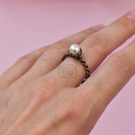 Ring with a pearl in the hands of a girl on a pink background