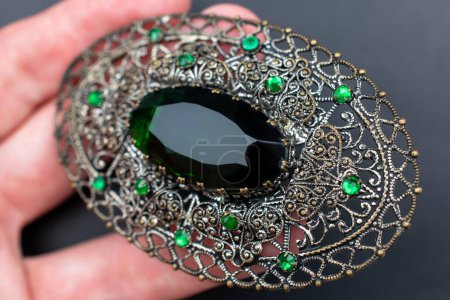 Hand holding a green sapphire brooch on a black background