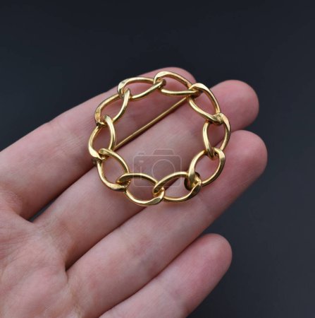Gold brooch in hand on a dark background. Jewelry and accessories.