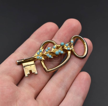 Hand holding a golden key on a dark background, close-up