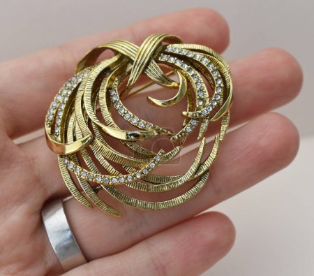 Beautiful gold brooch in hand on a gray background. Jewelry and accessories.