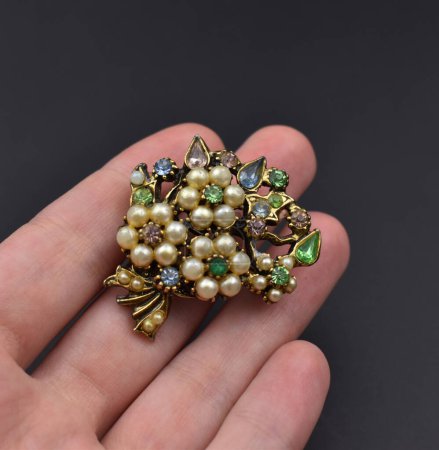 Hand holding a small brooch with precious stones on a dark background