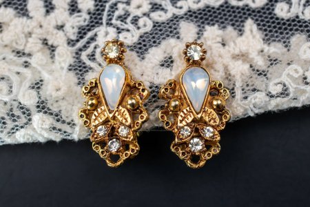 Golden earrings with precious stones on a black background with lace.