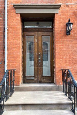 Wooden door in a red brick building with black railing and stairs