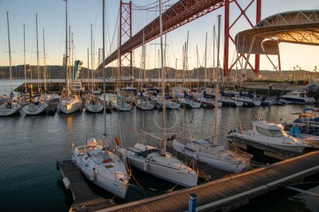 Photo for Lisbon, Portugal, Ponte 25 de Abril Bridge and mooring boats, sailboats at rest in the marina at sunset, modern architecture - Royalty Free Image